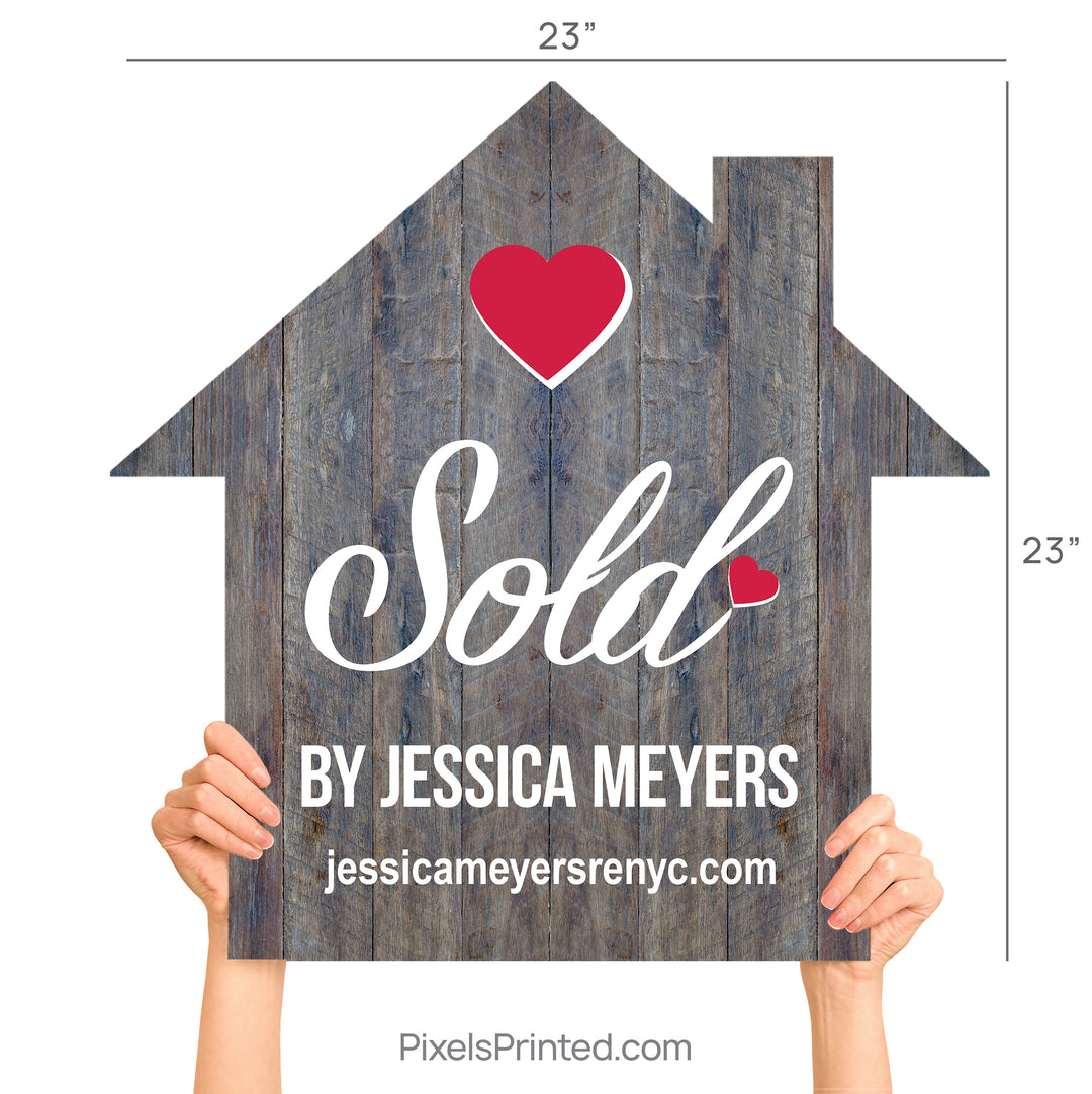 A realtor holding a wooden house-shaped sign that says Sold By during a client closing.